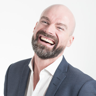 Smiling man in a suit and tie facing forward with a confident and friendly expression, set against a softly blurred professional background